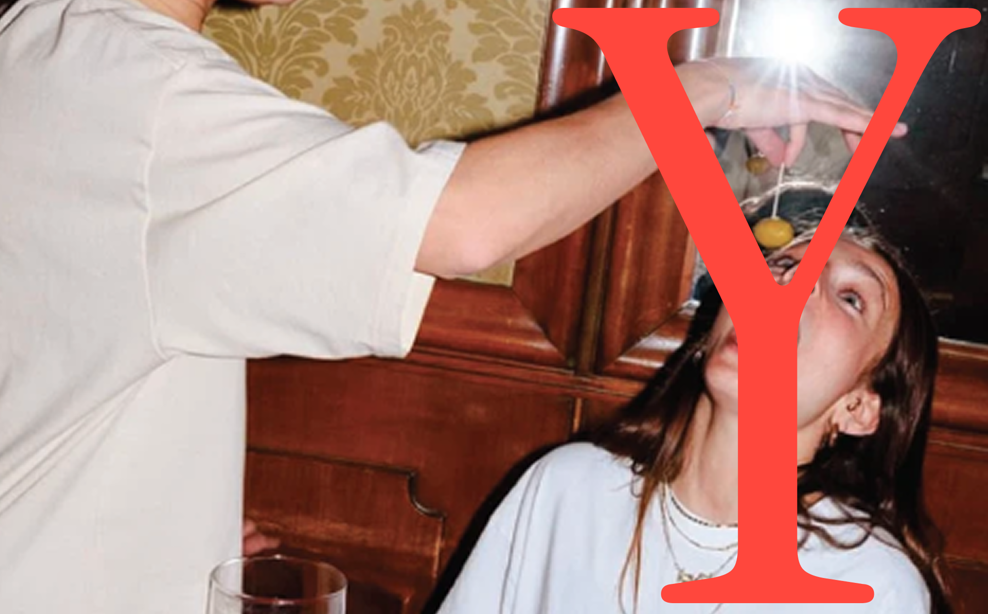 A large red Y over a photo of a woman being fed an olive in a bar